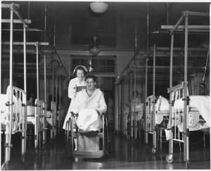 740px-Nurse_Frances_Bullock_wheels_a_wounded_soldier_back_to_his_bed_in_the_orthopedics_ward_of_an_Army_hospital._-_NARA_-_196365